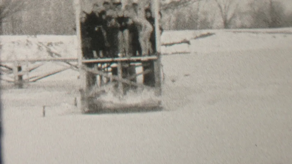 The diver has entered the water below the wooden dock, creating a visible splash while the group stays clustered on the snowy winter platform.