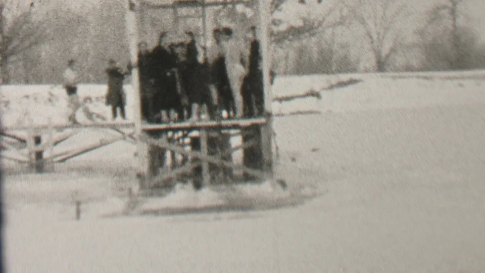 The frame shows a small winter-clad group on a wooden platform in the snowy Albany scene, with one figure standing apart near the waterline.