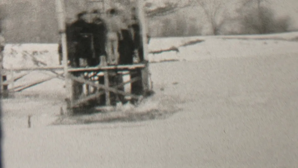In 1937 Albany home-movie footage, several bundled figures gather on a wooden lakeside platform with snow-covered ground and bare trees behind them.