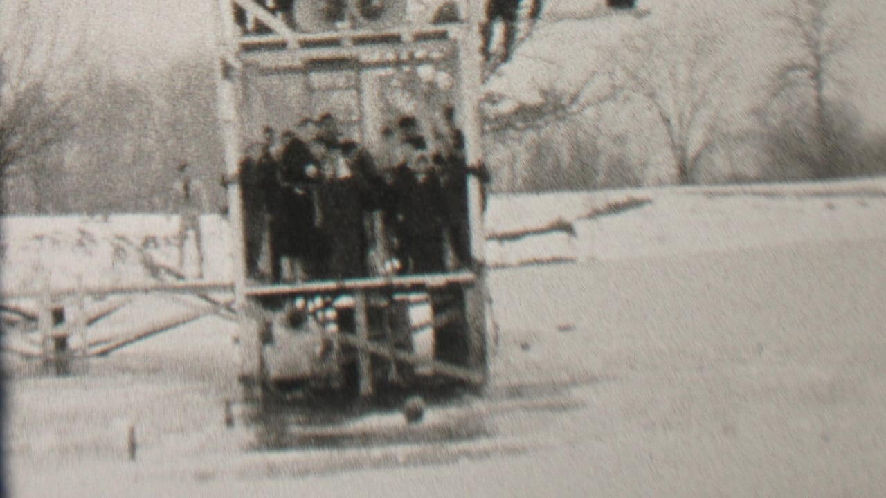Albany, New York home-movie frame from 1937 showing men in winter coats grouped on a wooden lakeside platform with snow and bare trees behind them.