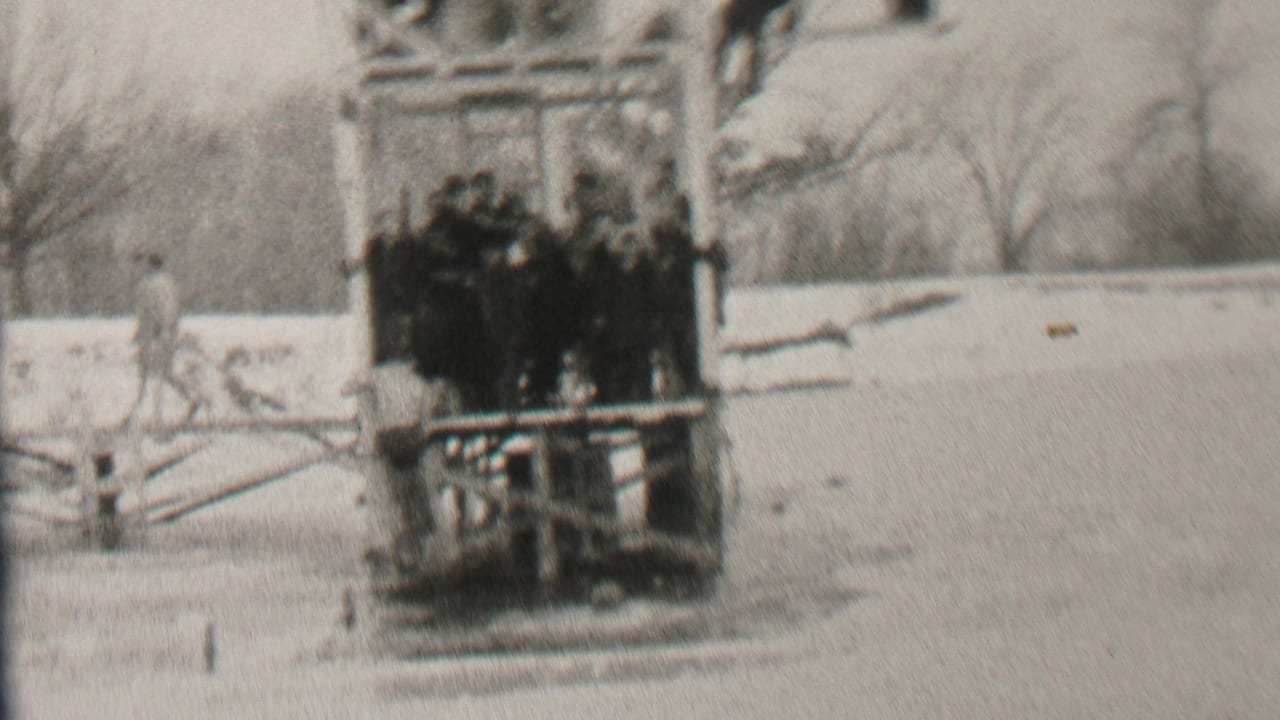 Albany, New York 1937 winter frame showing a clustered group of men on a wooden platform near a frozen lake, with another person walking across the snowy ground.