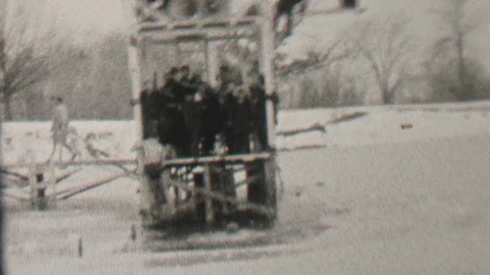 Albany, New York 1937 winter frame showing a clustered group of men on a wooden platform near a frozen lake, with another person walking across the snowy ground.