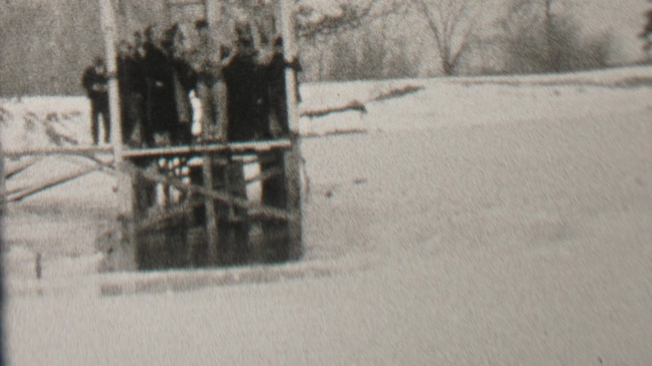 People clustered on a dock over a wintry lake with a snowy bank in the background.