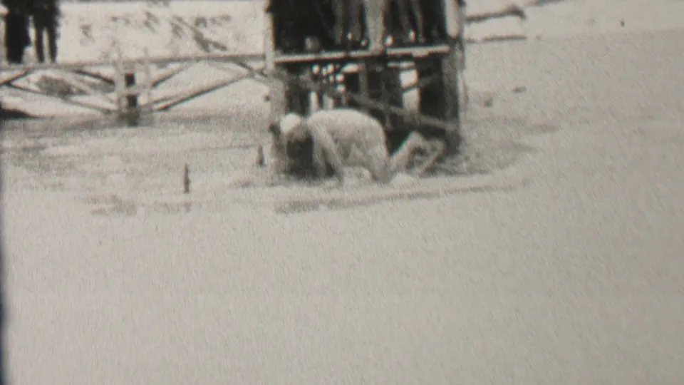 A lightly dressed swimmer appears to crouch or enter icy water beside the wooden platform while bundled spectators remain nearby in the snowy 1937 Albany scene.