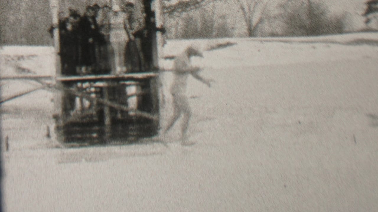 In 1937 Albany, New York home-movie footage, a swimsuit-clad man moves across ice beside a wooden platform where bundled spectators stand.