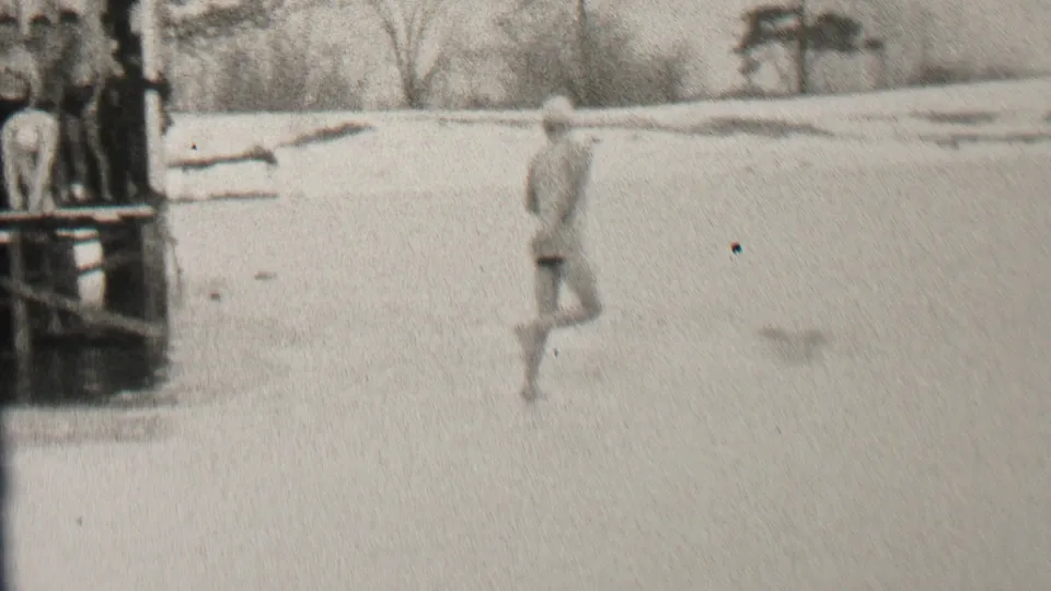 The swimmer continues across the frozen surface in the Albany winter scene, moving away from the platform and toward the open ice area.