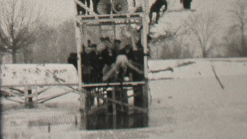 A young man appears to bend or climb near the lower part of the wooden lake structure as teammates stand inside it on the frozen Albany lake.