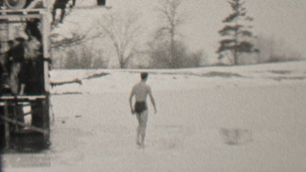 The Albany winter home-movie frame shows the swimmer walking across the ice as the dock and distant snow-covered shoreline remain in view.