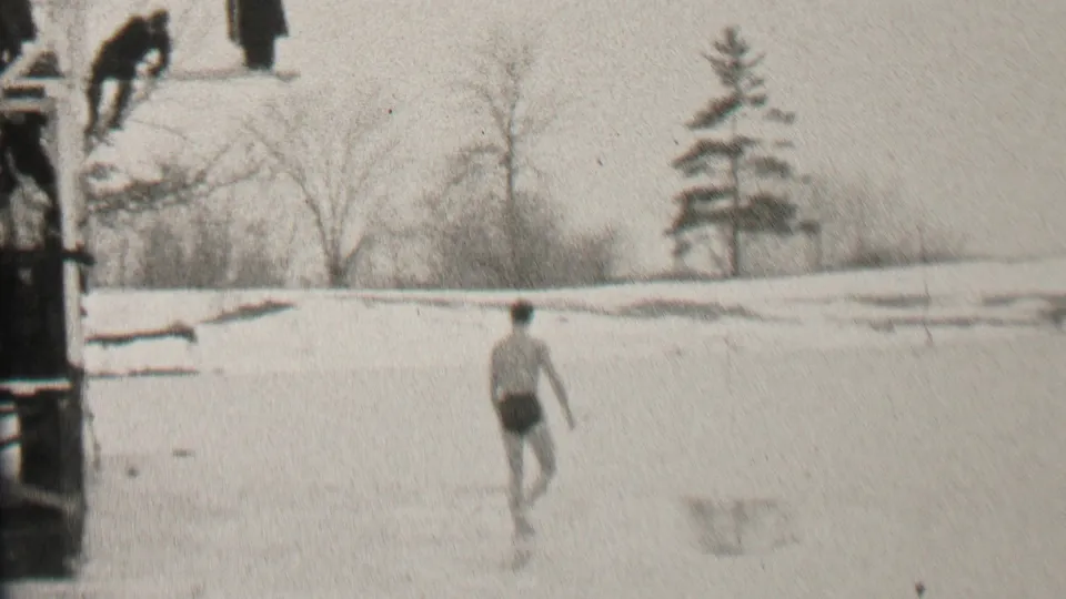The swimmer continues across the frozen surface in the 1937 Albany footage, with bare trees, snow, and part of the dock visible at the side.