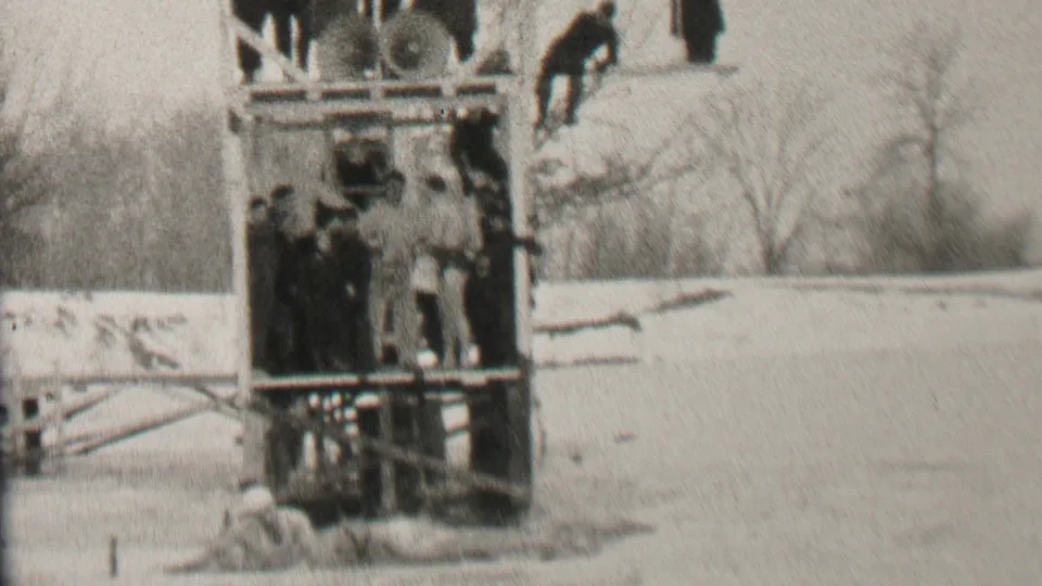 In the stated 1937 Albany, New York context, spectators in winter clothing gather on and around a wooden platform beside snow-covered ground and bare trees.
