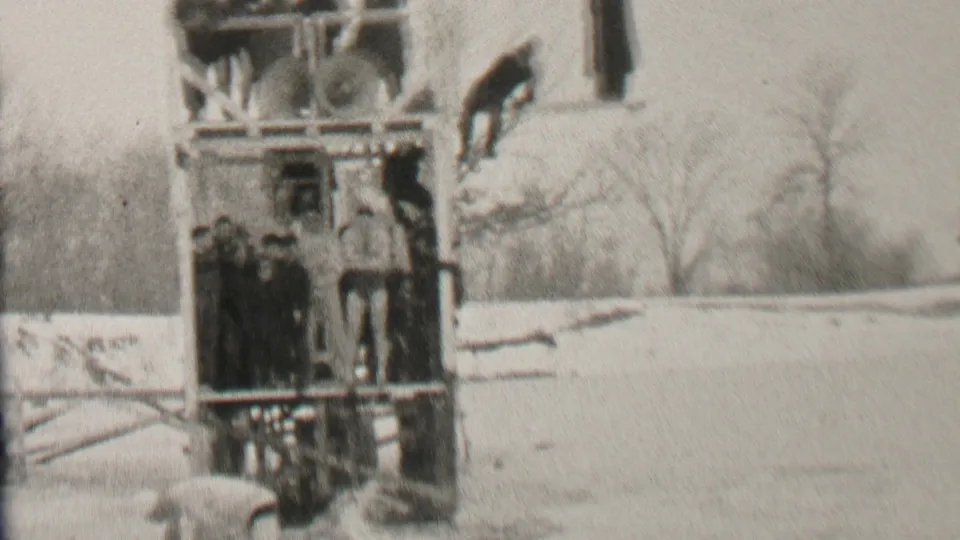 A swimmer or diver is visible near the upper board of a wooden winter platform as bundled spectators look on in the snowy Albany setting described by the clip metadata.
