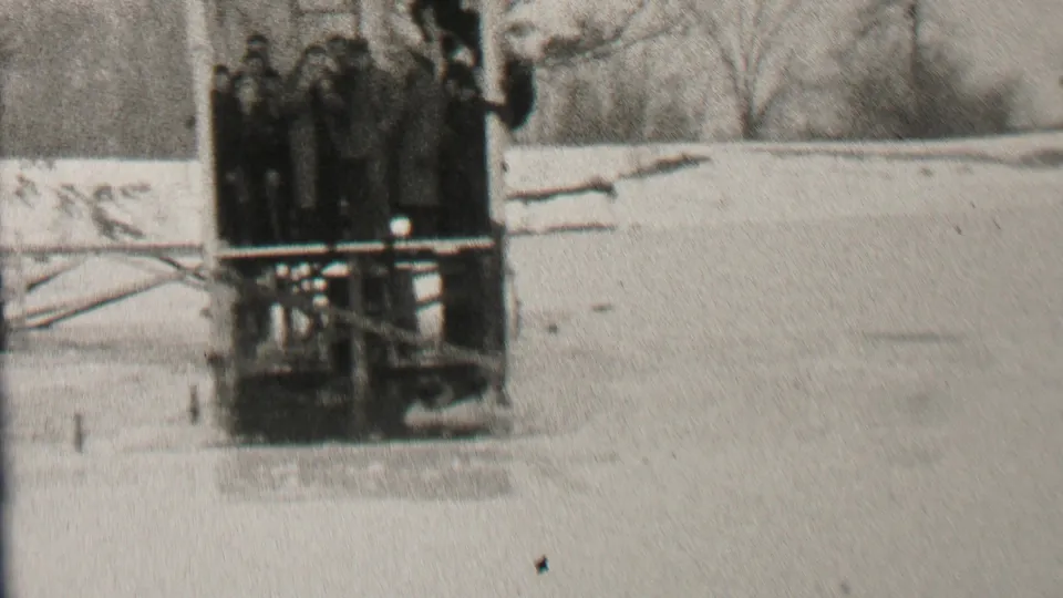 Bundled spectators remain packed on the wooden platform while the snowy frozen surface and bare winter trees fill the surrounding Albany scene.