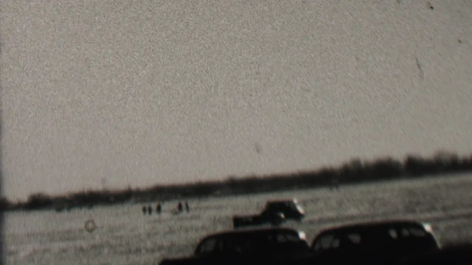 1937 Albany, New York 8mm frame showing dark early automobiles driving over an open field with small groups of observers in the distance.
