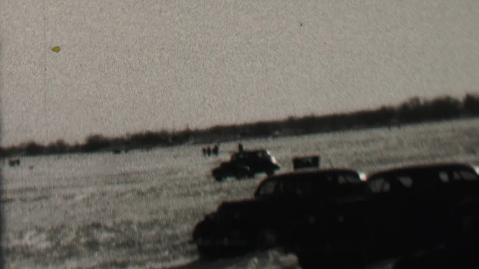 1937 Albany, New York 8mm frame with multiple dark automobiles on a broad field and distant people standing near the horizon line.