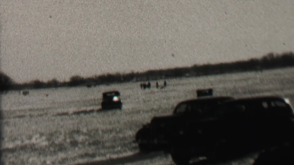 1937 Albany, New York 8mm frame showing a dark automobile close to the camera, another car farther out, and scattered observers across the open field.