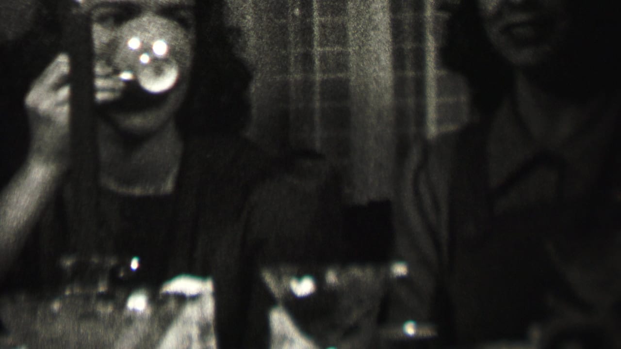 In 1937 Albany home-movie footage, a woman raises a cup toward her mouth at a dim dinner table while adult companions sit beside her.