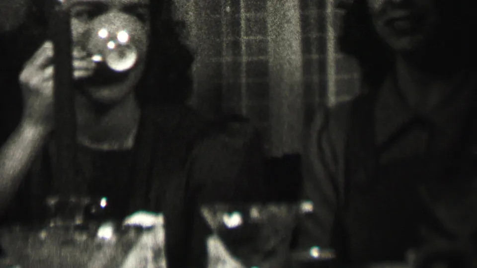 In 1937 Albany home-movie footage, a woman raises a cup toward her mouth at a dim dinner table while adult companions sit beside her.