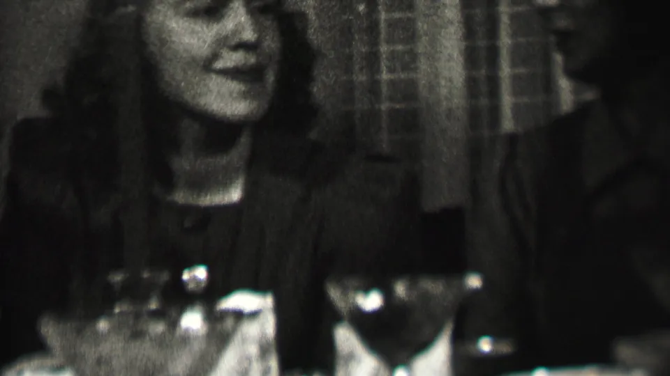 A smiling woman sits at a candlelit dining table in Albany, New York, with partially visible adult companions and table glassware around her.