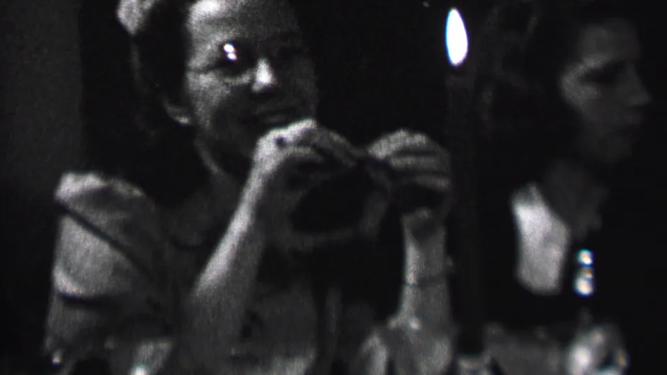 A woman in the 1937 Albany home-movie footage smiles in candlelight while seated near other women in a dark private interior.