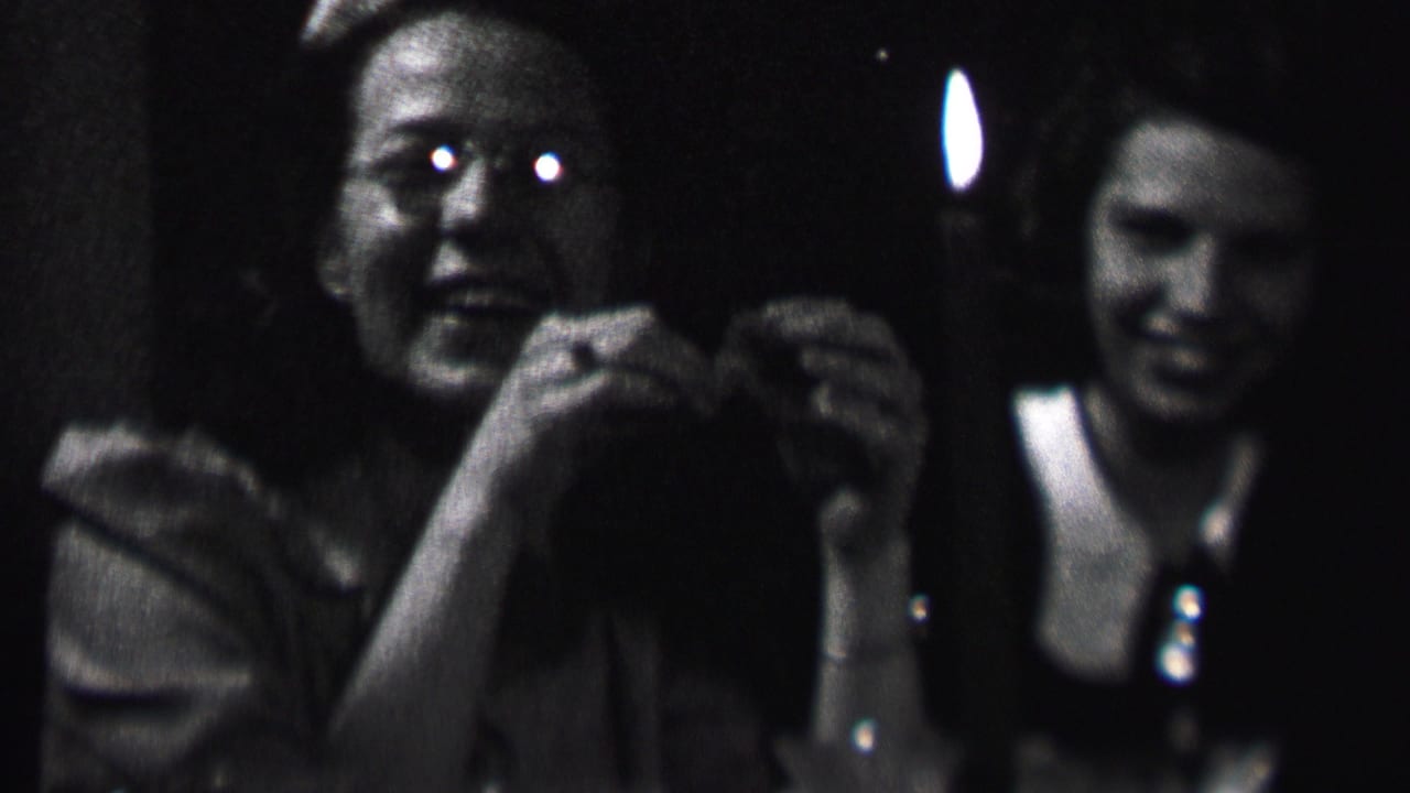 1937 Albany home-movie frame showing two young women at a candlelit indoor gathering, one facing the camera while another smiles in the background.