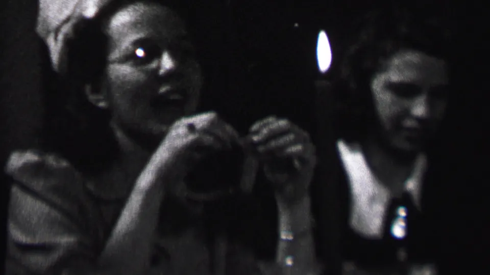 Black-and-white 8mm frame from Albany, 1937, with a young woman near the candle and another woman in a white-collared dress behind her.