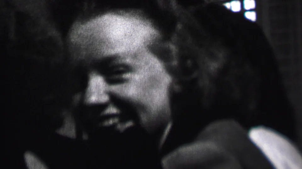 Black-and-white 8mm frame of a young woman laughing during the 1937 Albany indoor gathering, with another person partially visible at the edge of the frame.