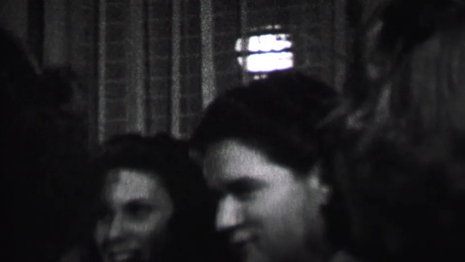 Black-and-white 1937 Albany home-movie frame showing several young women laughing and leaning together in a softly focused indoor social moment.