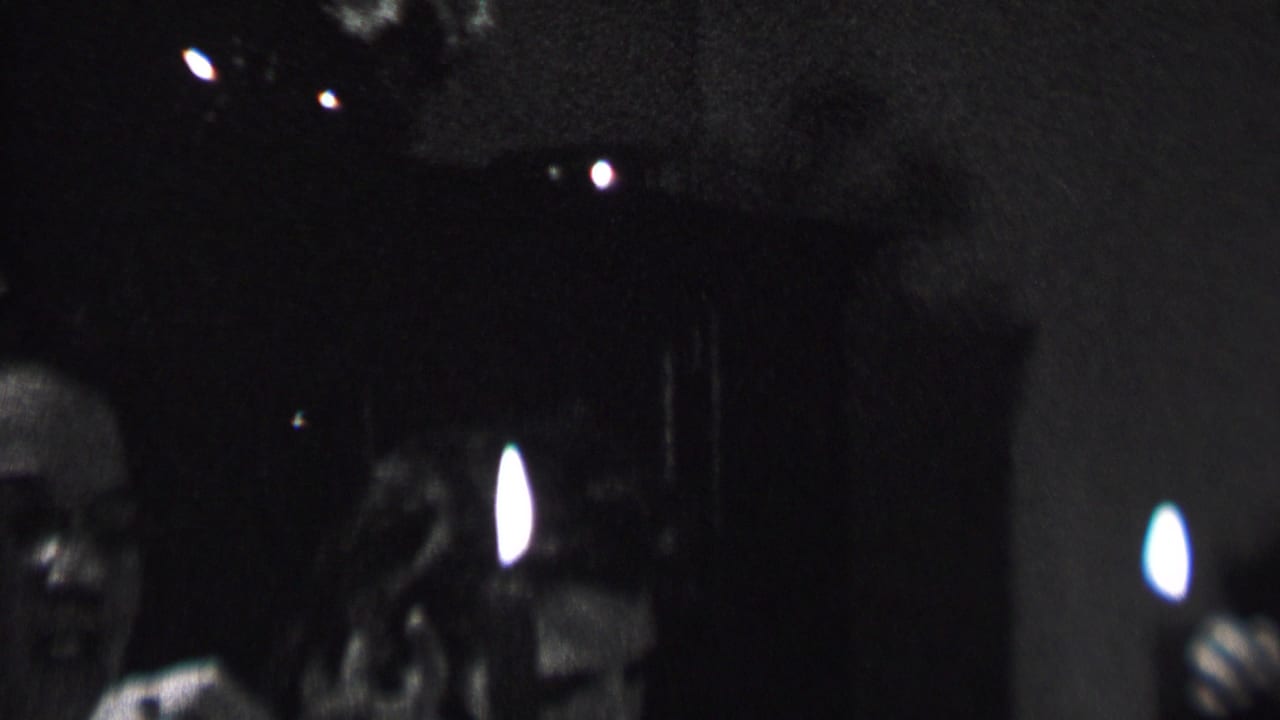 Two adult party guests in a dark room with a candle flame and curtains behind them.