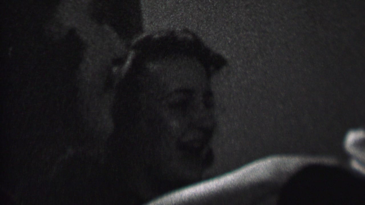 In 1937 Albany home-movie footage, two women appear in close-up at a dim indoor party, smiling and laughing as they face someone off camera.