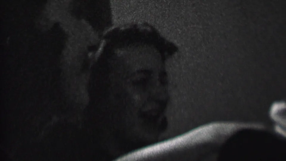 In 1937 Albany home-movie footage, two women appear in close-up at a dim indoor party, smiling and laughing as they face someone off camera.