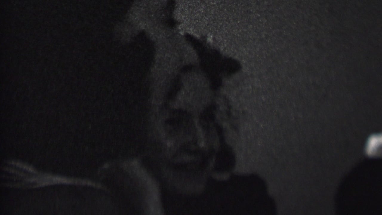 A woman laughs in profile beside another woman in a dark interior.