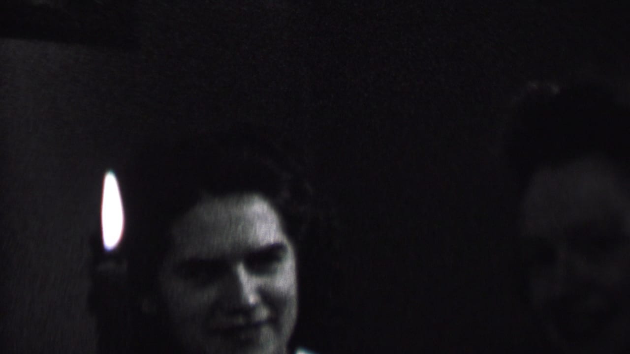 In this Albany, New York 1937 home-movie frame, a woman smiles near a candle flame in a very dim private interior.