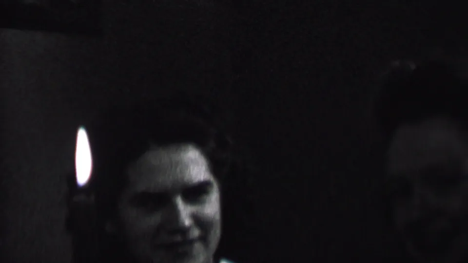 In this Albany, New York 1937 home-movie frame, a woman smiles near a candle flame in a very dim private interior.