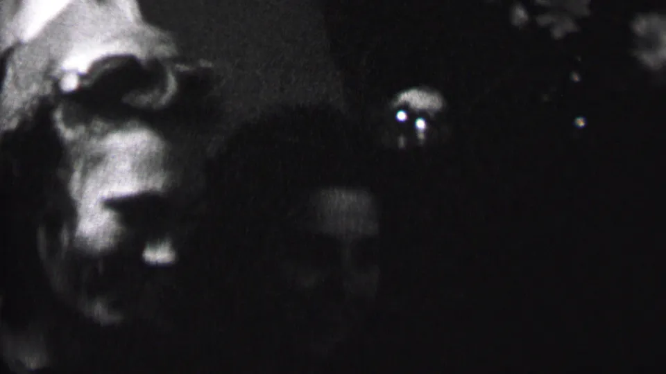 In this 1937 Albany home-movie frame, several women are seen close to the camera in a dim interior, including a visible pointed party hat and partially lit faces.