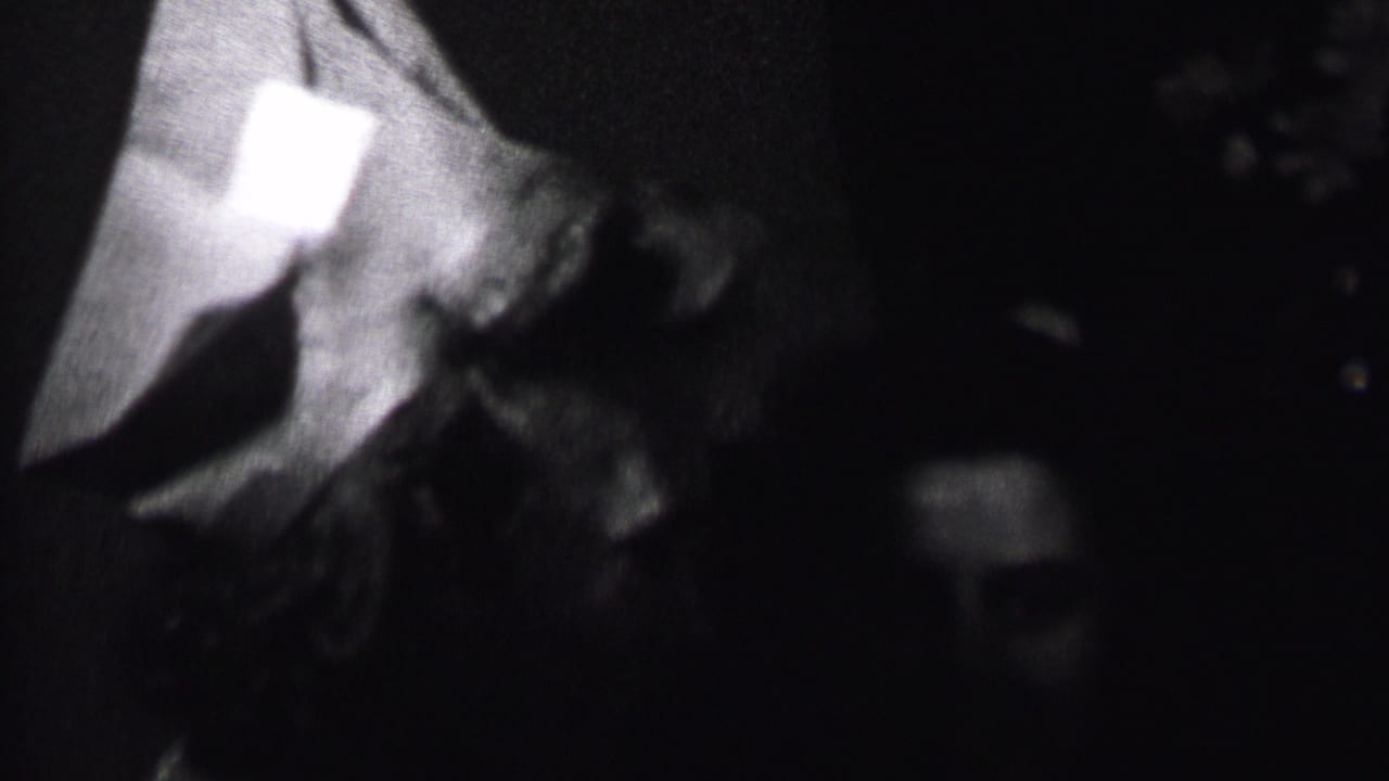 In supplied 1937 Albany home-movie footage, two adults appear close together in a dim interior while one wears a pointed party hat.