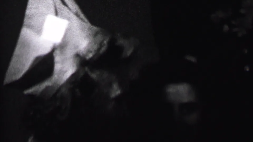In supplied 1937 Albany home-movie footage, two adults appear close together in a dim interior while one wears a pointed party hat.