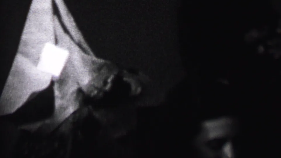 A dark, soft-focused 8mm frame shows a person in a pointed party hat leaning toward another adult in the Albany home-movie scene.