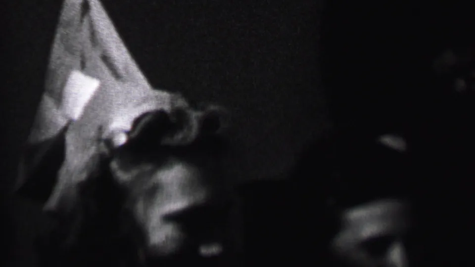 The 1937 home-movie frame shows two adults in shadow during a close indoor exchange, with the pointed party hat the clearest visible detail.