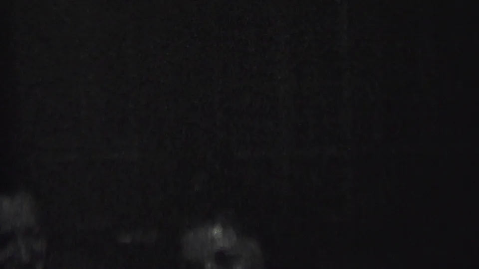 Low-light 8mm frame from the Albany 1937 clip with indistinct people or face-like silhouettes near the bottom and center of the image.