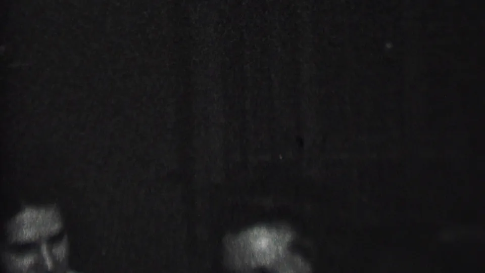 Dim black-and-white home-movie frame with a partial face or head near the lower left and little visible setting detail.