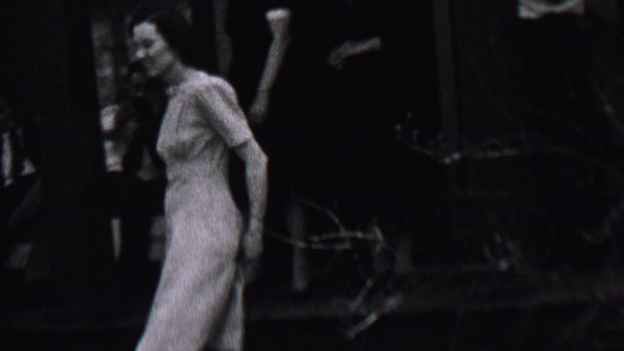 Woman in a light dress walking near a dark parked car and trees.