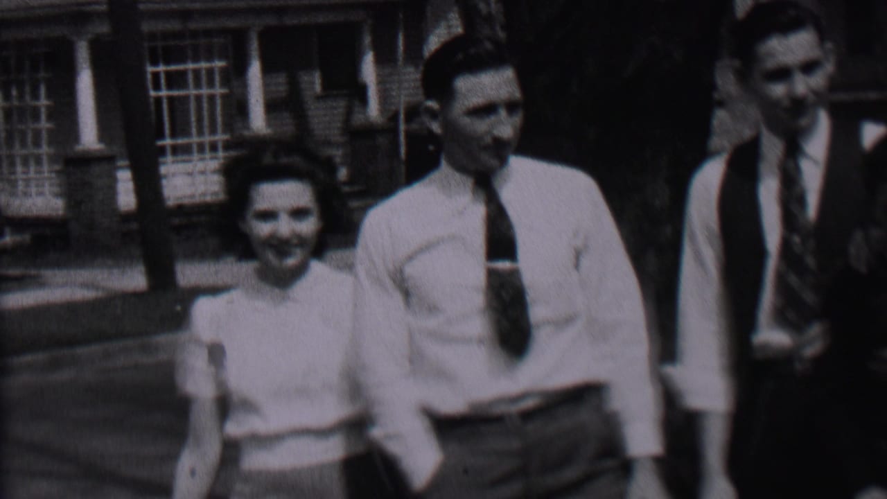 In 1937 Albany home-movie footage, a woman in a light blouse walks toward two men in shirts and ties near a brick residential-looking building.