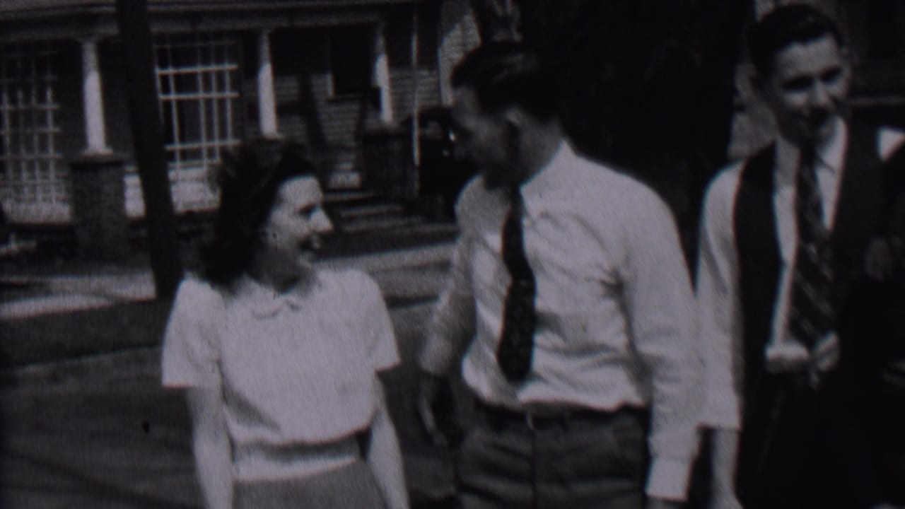 Woman smiles toward a man in a white shirt and tie as another man stands nearby.