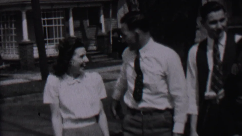 In the Albany street scene, the woman smiles at a man in a white shirt and dark tie while a second man in a vest watches from behind.