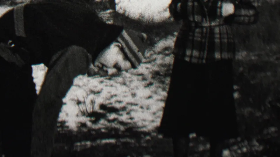 The frame shows a dark-clothed adult bending over snowy ground with the plaid-coated woman partly cropped at center in the Beachwood, New Jersey winter home movie.