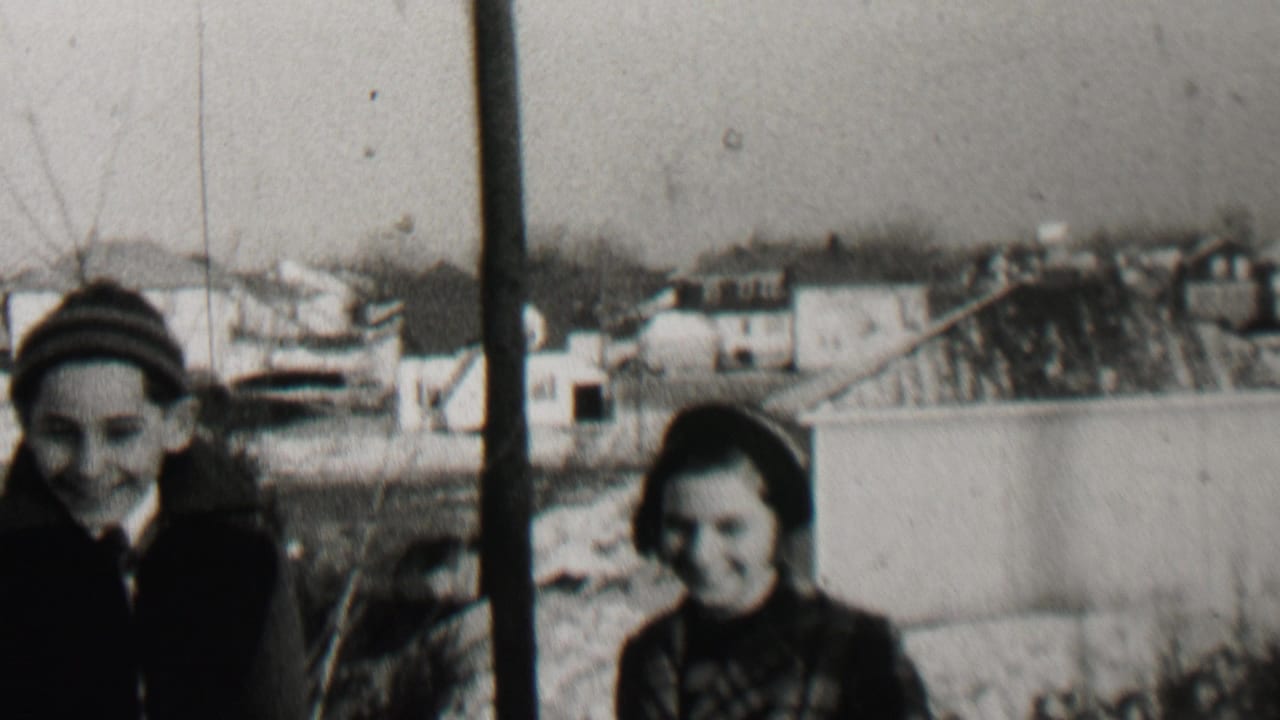 Two children stand near a pole in a winter yard with houses in the background.