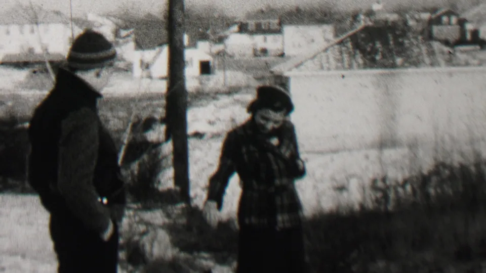 The woman appears to gesture or speak while standing near the man in a winter residential setting in the 1937 Beachwood, New Jersey home-movie footage.