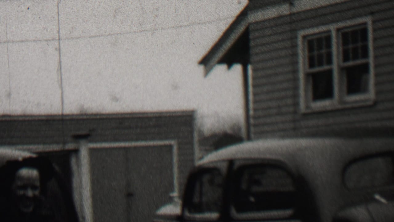 1937 Beachwood, New Jersey home-movie frame showing adults near a clapboard-sided residence, a garage, and a rounded automobile in the foreground.