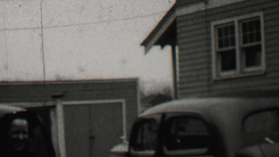 1937 Beachwood, New Jersey home-movie frame showing adults near a clapboard-sided residence, a garage, and a rounded automobile in the foreground.