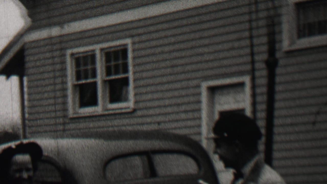 Man and woman partly visible in front of a house and parked car.